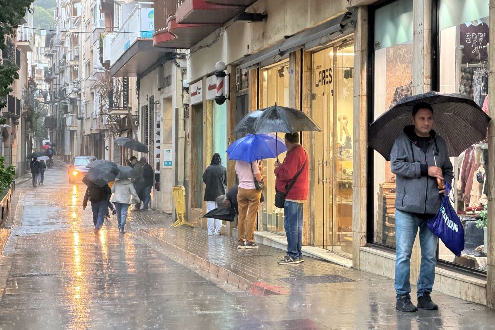 Pluja i gent amb paraigües a l'eix comercial de Blanes