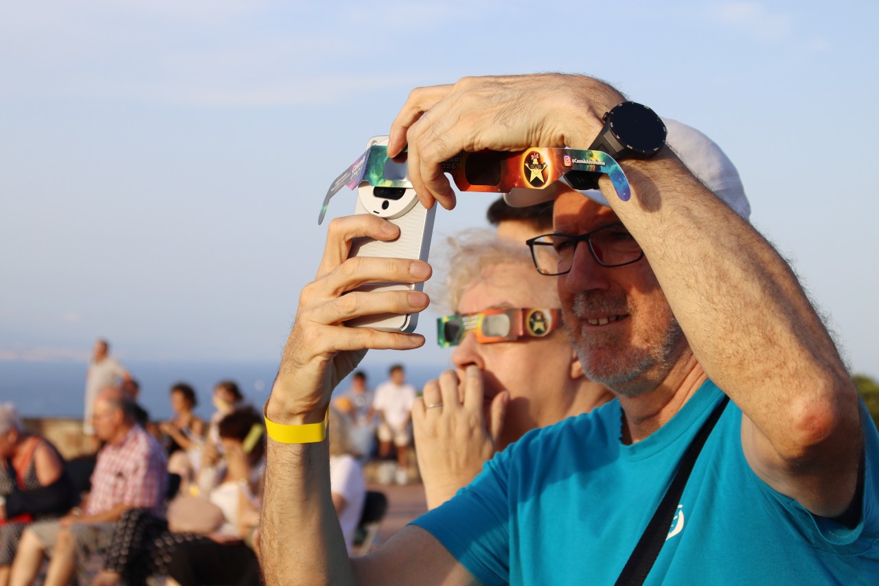 Un home fotografia l'eclipsi amb el seu mòbil i les ulleres homologades des del Castell de Montjuïc.