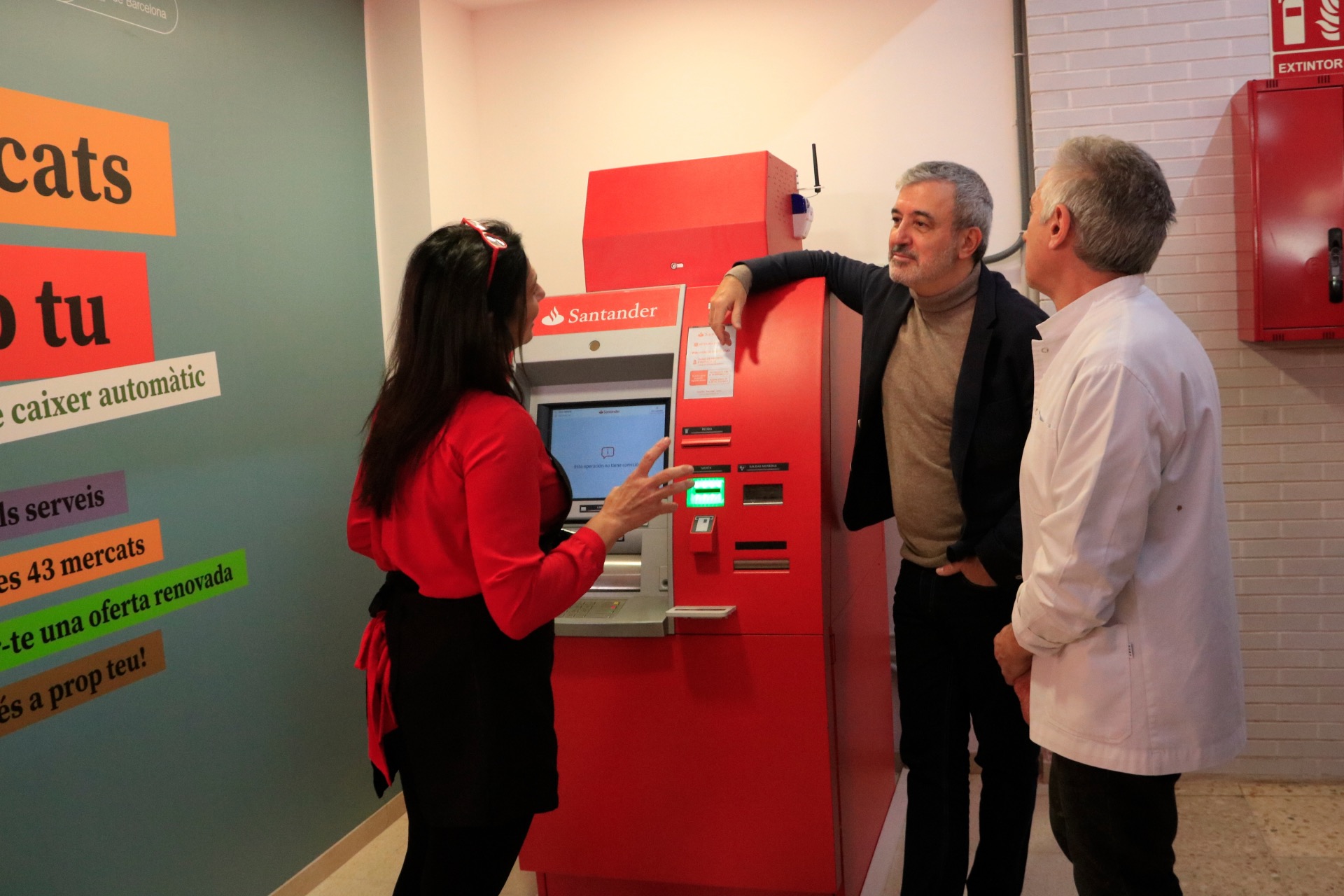 El tinent d'alcaldia d'Economia de Barcelona, Jaume Collboni, amb el president del Mercat del Besòs, Joaquim Tomás, i la propietària d'una parada de llegums, Lourdes Mulero, amb el caixer bancari instal·lat en aquest equipament.